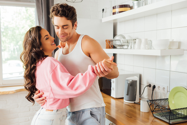 Smiling young man dancing with beautiful girlfriend in kitchen  - Fotoğraf, Görsel