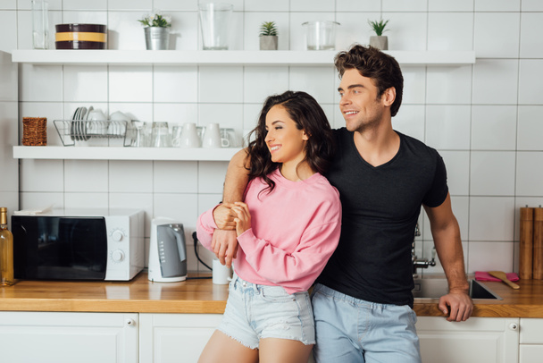 Smiling man embracing beautiful woman near worktop in kitchen at home  - Photo, image