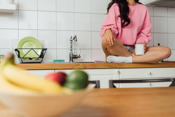 Rajattu näkymä nuori nainen tilalla kuppi kahvia työtasolla keittiössä  - Valokuva, kuva