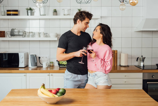 Выборочный фокус улыбающейся девушки, звенящей вином с красивым парнем на кухне  - Фото, изображение
