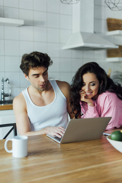 Selectieve focus van lachende vrouw kijken naar laptop in de buurt vriendje in de keuken  - Foto, afbeelding