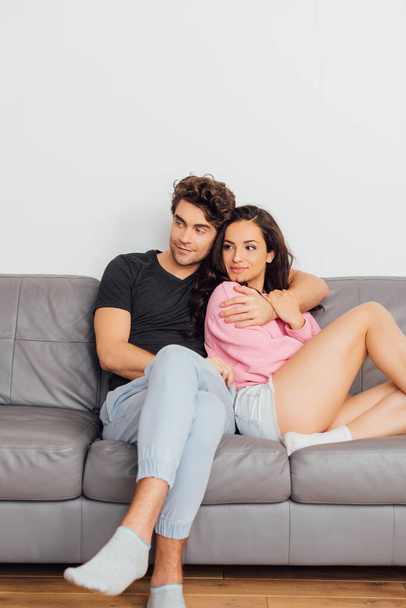 Selective focus of handsome man embracing beautiful girlfriend on sofa at home  - Фото, изображение