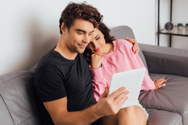 Selective focus of young couple using digital tablet in living room - 写真・画像