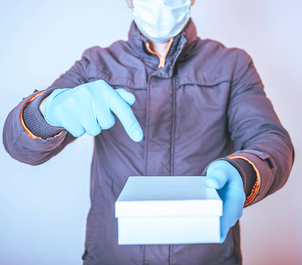 Courier in protective mask delivers parcel to client. Delivery service under quarantine, disease outbreak, coronavirus covid-19 pandemic conditions. Stay home and shopping online. - Foto, afbeelding