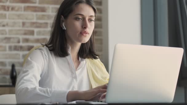 Young gorgeous concentrated business woman indoors at home using laptop computer in wireless earphones - Filmmaterial, Video