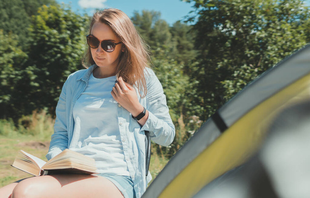 湖のそばのテントで本を読んでいる女. - 写真・画像