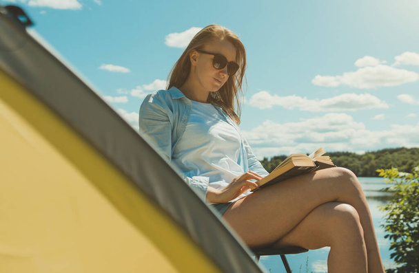 Женщина, читающая книгу у палатки у озера. - Фото, изображение