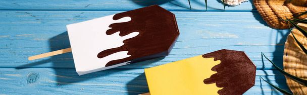 top view of seashells and palm leaves near ice cream on wooden blue background, panoramic shot - 写真・画像
