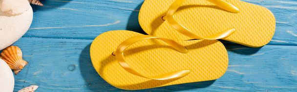top view of yellow flip flops near seashells and stones on wooden blue background, panoramic shot - Photo, Image