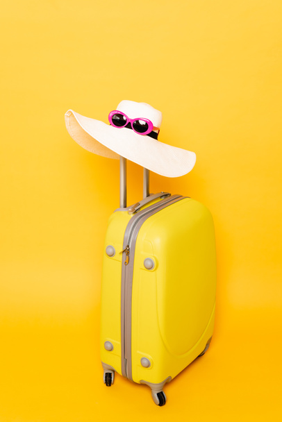 sun hat and sunglasses on suitcase handle on yellow background - Foto, Bild