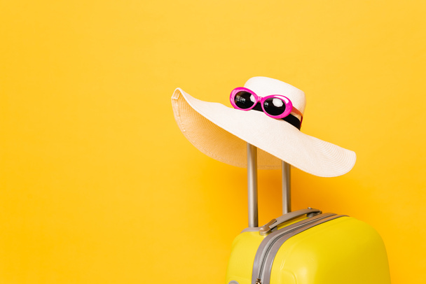 sluneční klobouk a sluneční brýle na rukojeti kufru na žlutém pozadí - Fotografie, Obrázek