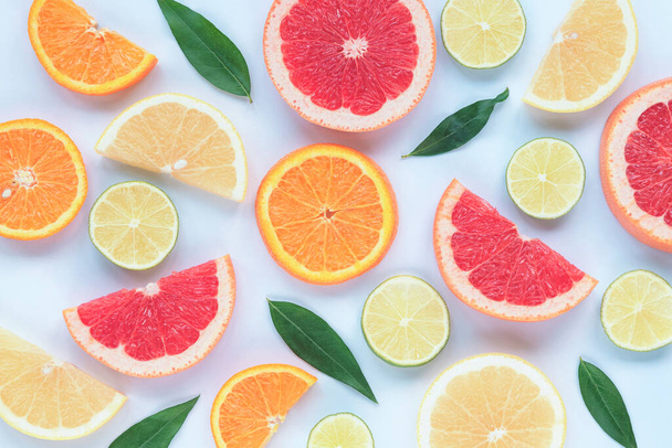 Çeşitli dilimlenmiş turunçgil meyveleri: kireç, turuncu, kırmızı ve sarı greyfurt, beyaz arka planda yeşil yapraklar, doku. - Fotoğraf, Görsel