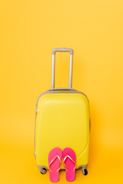 τσάντα ταξιδίου με ροζ σαγιονάρες που απομονώνονται σε κίτρινο φόντο - Φωτογραφία, εικόνα