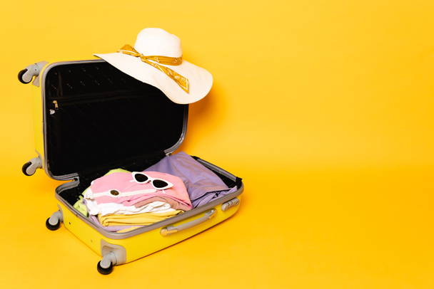 open travel bag with summer clothes and accessories on yellow background - Φωτογραφία, εικόνα