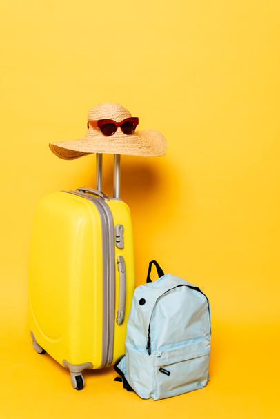 сумка с солнцезащитной шляпой и солнцезащитными очками возле рюкзака на желтом фоне - Фото, изображение
