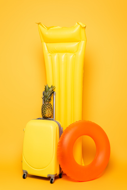 travel bag with pineapple near pool floats on yellow background - Φωτογραφία, εικόνα