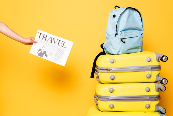 vista cortada de mulher segurando jornal de viagem perto de mochila azul em sacos de viagem em amarelo
 - Foto, Imagem