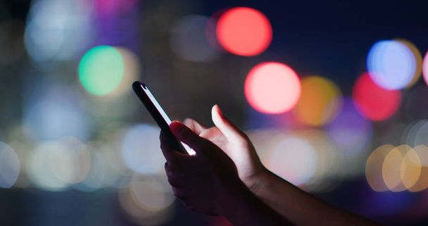 Жінка використовує смартфон на фоні міської ночі
 - Фото, зображення