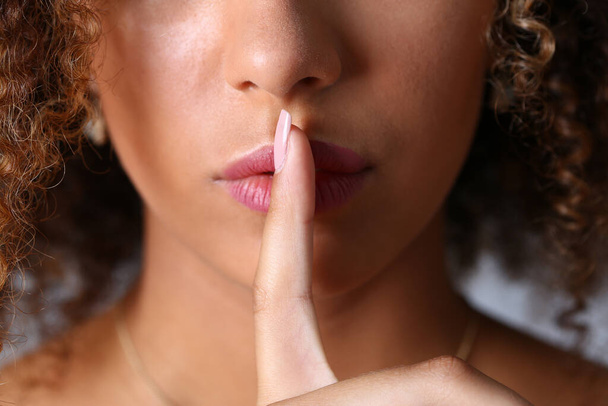 krullend jong vrouw houden index vinger op lippen - Foto, afbeelding