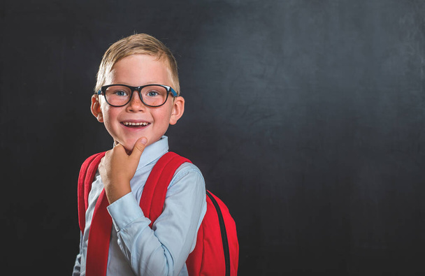 Portret van een schooljongen met rugzak tegen schoolbord. Leerling in uniform gaat terug naar school - Foto, afbeelding