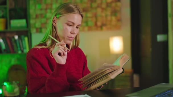 Dobře vypadající žena čte knihu v knihovně studovat něco pro její vysokoškolský projekt před kamerou - Záběry, video