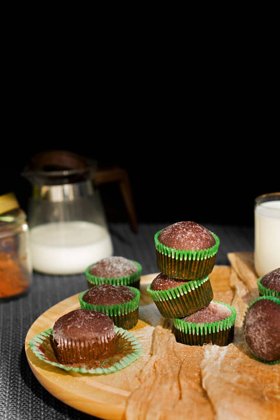 Chocolate muffins on a dark background. Powdered sugar muffins. Cupcakes with milk. Bakery products. - Фото, изображение
