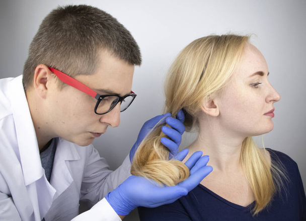 Un médecin trichologue effectue une étude des cheveux d'une blonde. Traitement d'alopécie. Perte de cheveux, alopécie, démangeaisons, brûlures dans la tête, séborrhée ou extrémités cassantes - Photo, image