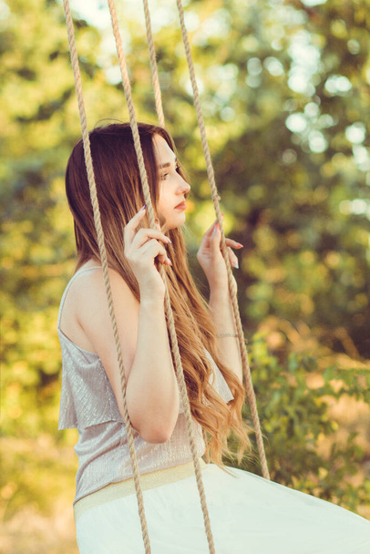 beautiful girl with long hair swinging on rope swing on summer nature, young woman relaxing, leisure activity, lifestyle concept - Foto, imagen