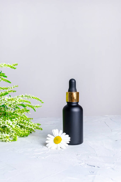 Composition from a black matte bottle with a dropper, chamomile and meadow flowers.. Natural cosmetics and skin care. Aroma essential oil - Fotografie, Obrázek