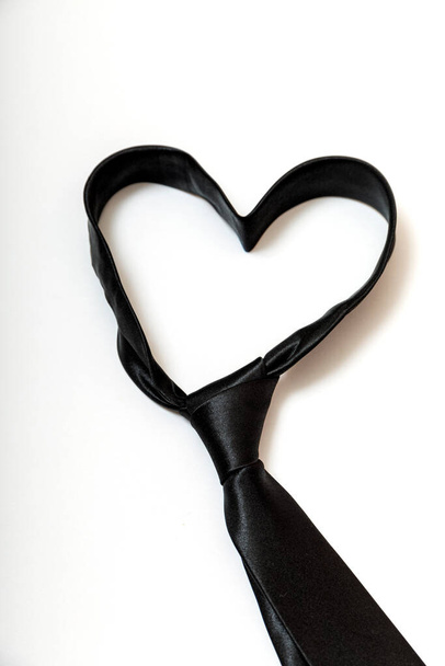 Zwarte stropdas vormt een hartvormige voor vaderdag achtergrond. Minimaal ontwerp op wit met kopieerruimte voor tekst. Hoge resultaatwaarde. - Foto, afbeelding