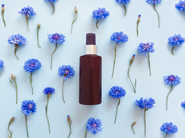 Mock-up of unbranded brown plastic spray bottle and blue cornflowers on a pastel blue background. Cosmetic bottle container for branding of medicine or cosmetics. Natural organic spa Body mist. - Photo, Image