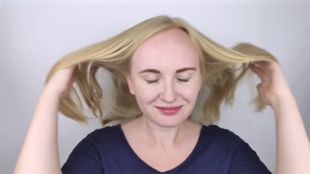 Φυσική ξανθιά πετάει και χνούδι μαλλιά της μπροστά από την κάμερα. Η έννοια της σωστής περιποίησης μαλλιών. Αργή κίνηση - Πλάνα, βίντεο