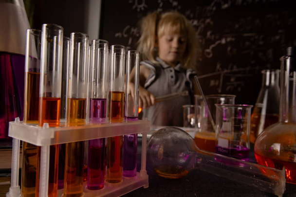 Ciekawa dziewczynka z probówkami i kolorowymi substancjami robi testy w szkolnym laboratorium. Mały dzieciak uczy się chemii. Wybiórcze skupienie. Koncepcja edukacji biologicznej. - Zdjęcie, obraz