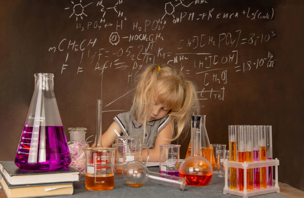 試験管とカラフルな物質を持つ好奇心旺盛な少女は、学校の実験室でテストを行います。小さな子供は化学を学び、生物学の授業で科学実験を行う。生物学教育の概念. - 写真・画像