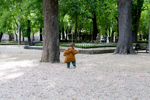 Um ano e meio de idade bebê dando seus primeiros passos em um parque com um piso de pedra solta, ele está aprendendo a andar
 - Foto, Imagem