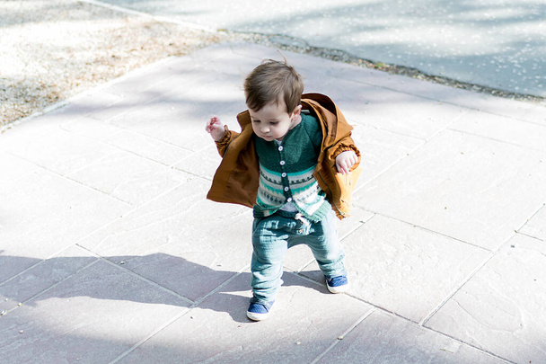 A year and a half old baby taking his first steps in a park with a loose stone floor, he is learning to walk - Photo, Image
