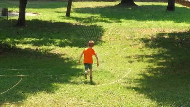 νεαρό αγόρι παίζει το καλοκαίρι κάτω από τις πιτσιλιές του νερού - Πλάνα, βίντεο