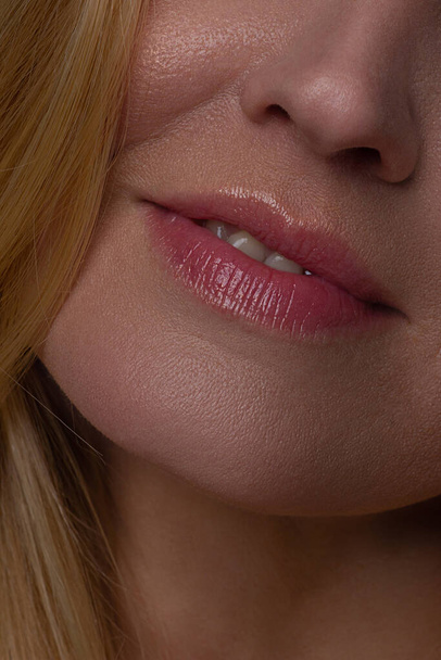 Cosmetics, makeup and trends. Bright lip gloss and lipstick on lips. Closeup of beautiful female mouth with natural lip makeup. Beautiful part of female face. Perfect clean skin in red light - Foto, afbeelding