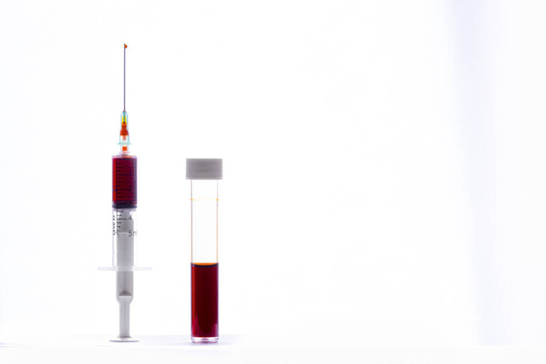 İçinde kan olan bir şırınga iğnede bir damla kan ve beyaz arka planda bir kan testi tüpü. - Fotoğraf, Görsel