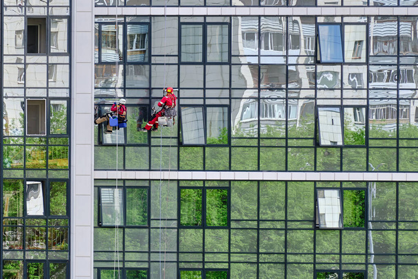 Dois alpinistas industriais do serviço de limpeza lavam a fachada de vidro de um moderno prédio de apartamentos. Acesso à corda
 - Foto, Imagem