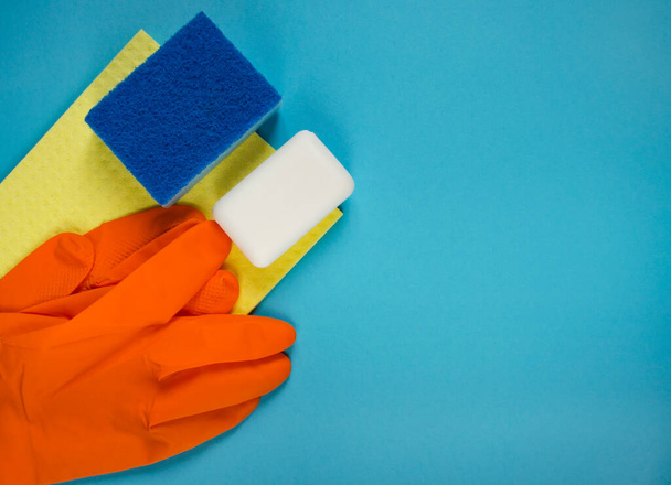 Rubber gloves, sponges and soap bar top view. Advertising banner for cleaning company with copy space. Protective gloves with washcloth on blue background. - 写真・画像