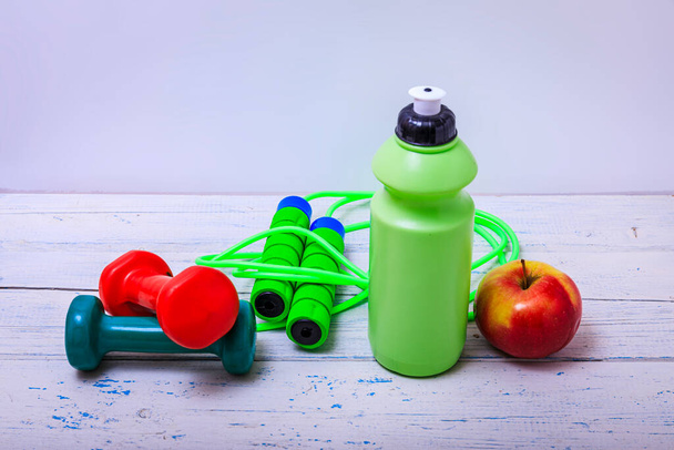 Green bottle of water, sports towel and exercise equipment isolated against a white background and wooden table. High resulotion image. - Photo, Image