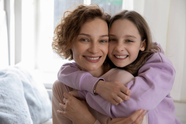 Головний знімок портрет усміхненої дочки-підлітка, що обіймає матір ззаду
 - Фото, зображення