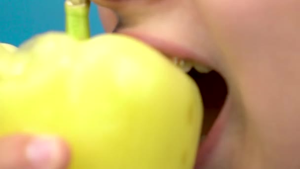 Adolescente com aparelho nos dentes come pimentão em um fundo azul. Uma menina com aparelhos coloridos morde um close-up de pimentão
. - Filmagem, Vídeo