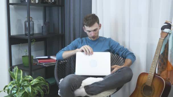 Young man starting to work on laptop computer from home office. Male working on laptop on chair. Work from home. Stay home. Businessman works from home on laptop on cozy chair in modern apartment - Záběry, video