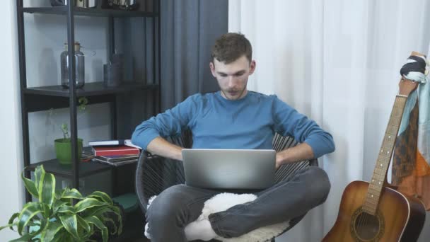 Young male freelancer finish to work on laptop computer at home office. Man relaxing on chair in modern apartment. Businessman works on notebook in chair.  Male programmer working on laptop at home - Metraje, vídeo