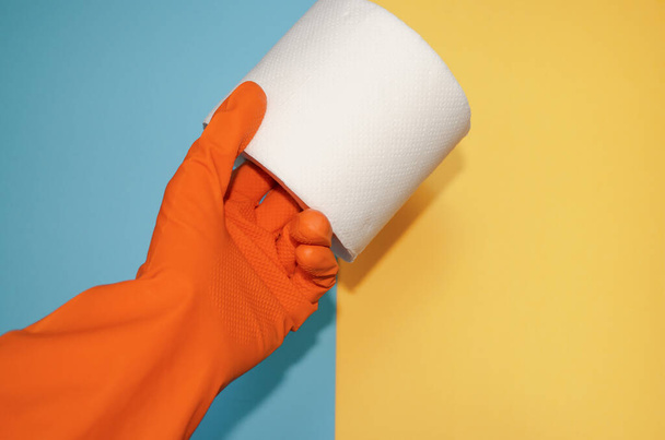 Ręka w rękawicy ochronnej trzyma papier toaletowy. Baner z dodatkiem środków higienicznych i środków do pielęgnacji ciała do codziennego użytku. - Zdjęcie, obraz