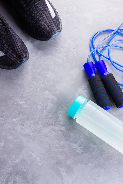Fitness concept with sneakers, jump rope and bottle of water. Sports equipment on a gray background. Healthy lifestyle concept. Copy space. Top view - Photo, Image