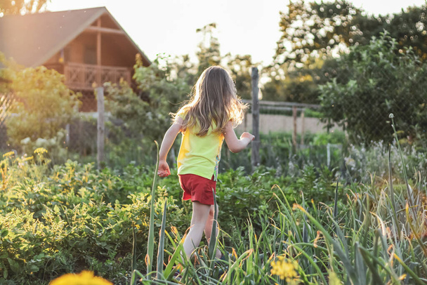 Kleines Mädchen mit lockeren Haaren läuft durch den Garten im Dorf - Foto, Bild