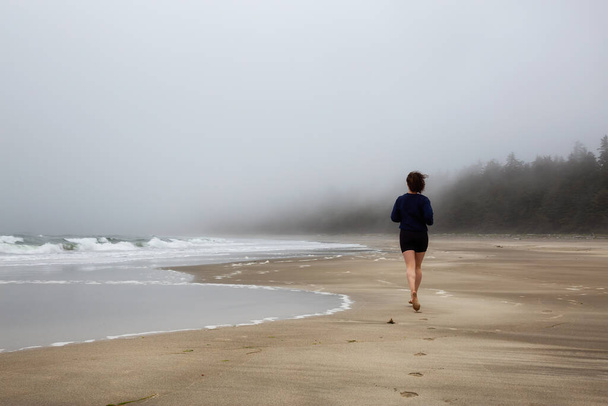 Athletic Caucasian Girl Running on a Sandy Beach near Pacific Ocean Coast - 写真・画像